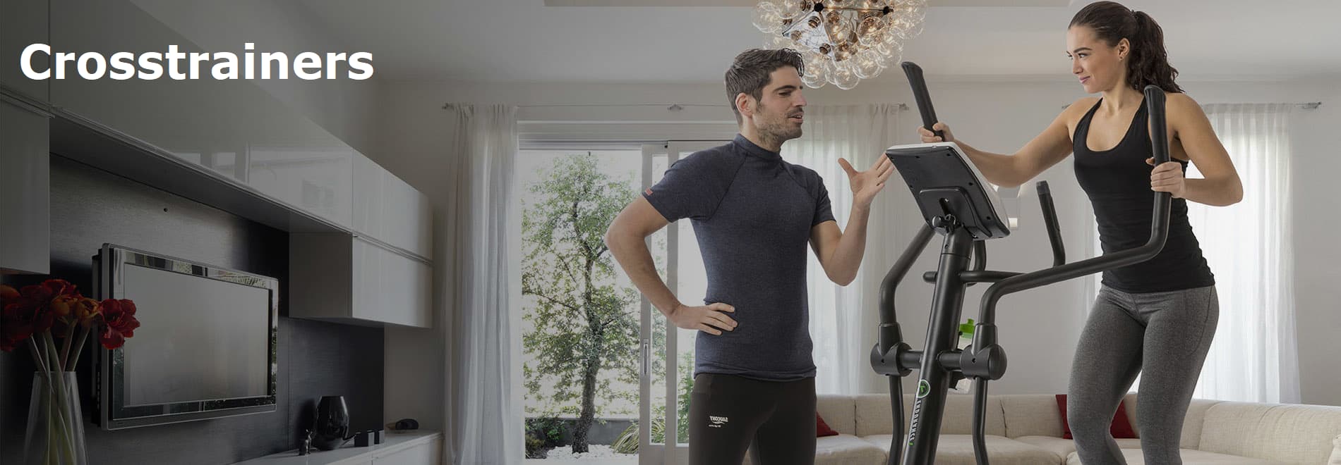 Dame op crosstrainer, heer naast de trainer geeft instructie